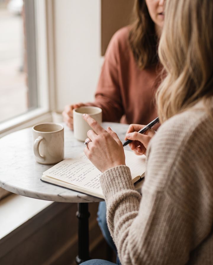 Two people talking over coffee with an open notebook of handwritten notes
