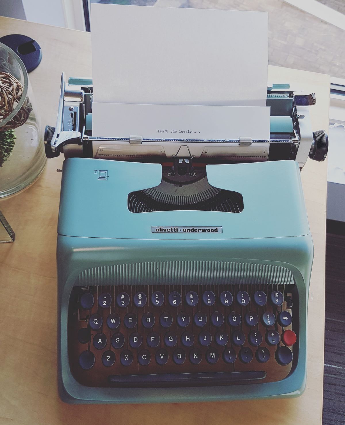 A mint green vintage typewriter with a sheet of paper loaded, on a wooden desk