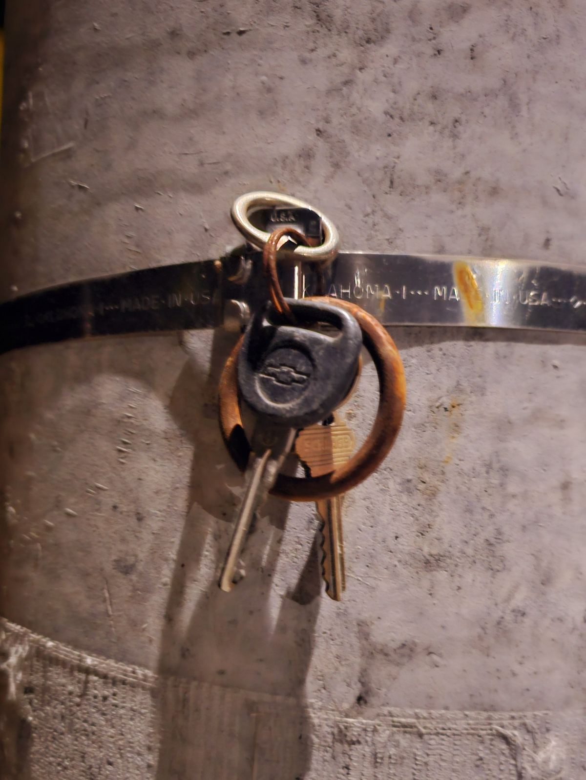 A ring of rusted keys hanging from a metal band on a concrete post